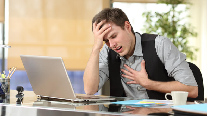 Businessman suffering an anxiety attack with the hands in his chest and head sitting in a desktop at office