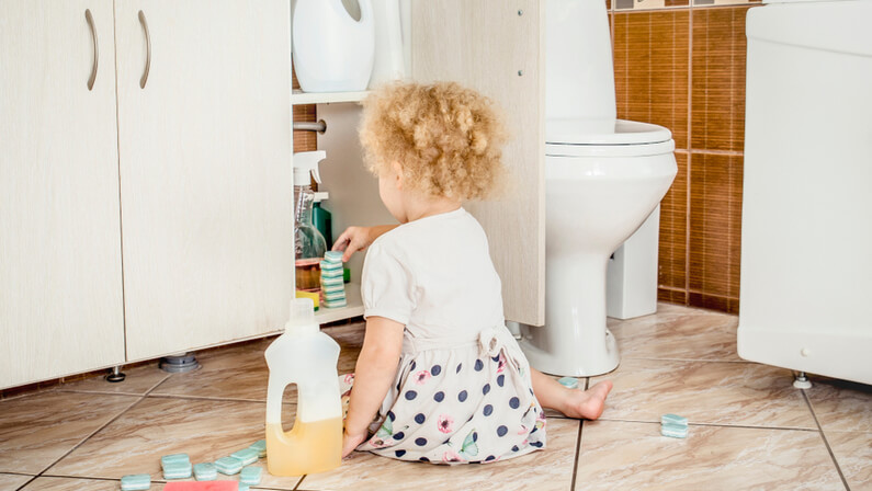 Unattended girl child play quietly at bathroom with dangerous household chemicals