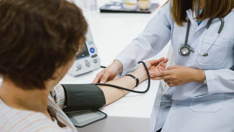 Young female doctor checking senior patient blood pressure.