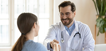 Smiling young Caucasian male doctor shake hand greeting get acquainted with female patient in hospital, happy man physician handshake woman client make agreement sign health insurance in clinic