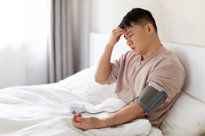 Unhealthy asian man wearing pajamas sitting in bed at home