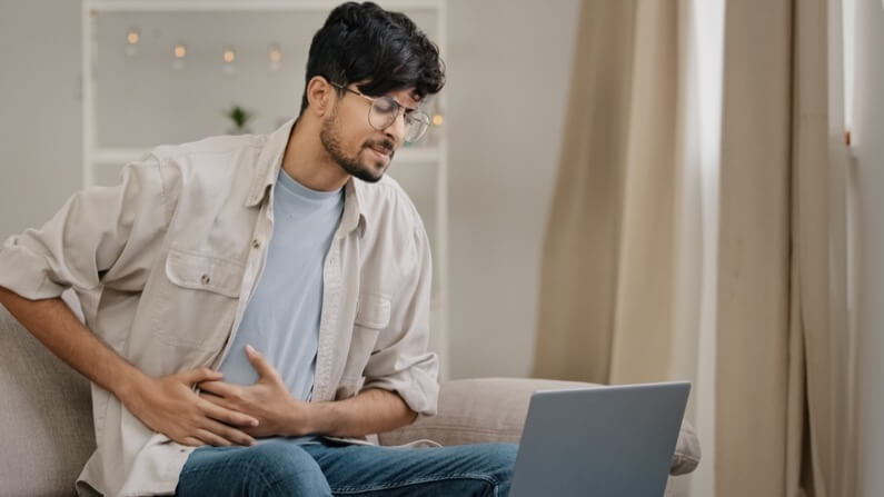 Young guy freelance business man at home working with laptop feels pain