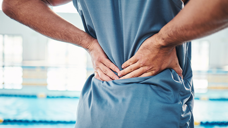 Back pain, sports and hands of man by swimming pool with injury, muscle ache and inflammation. Wellness, support and athlete with accident, health problem or bruise from fitness, exercise or training