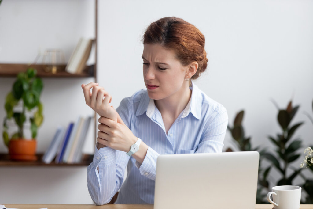 Businesswoman sitting at desk in office touch wrist feels pain.