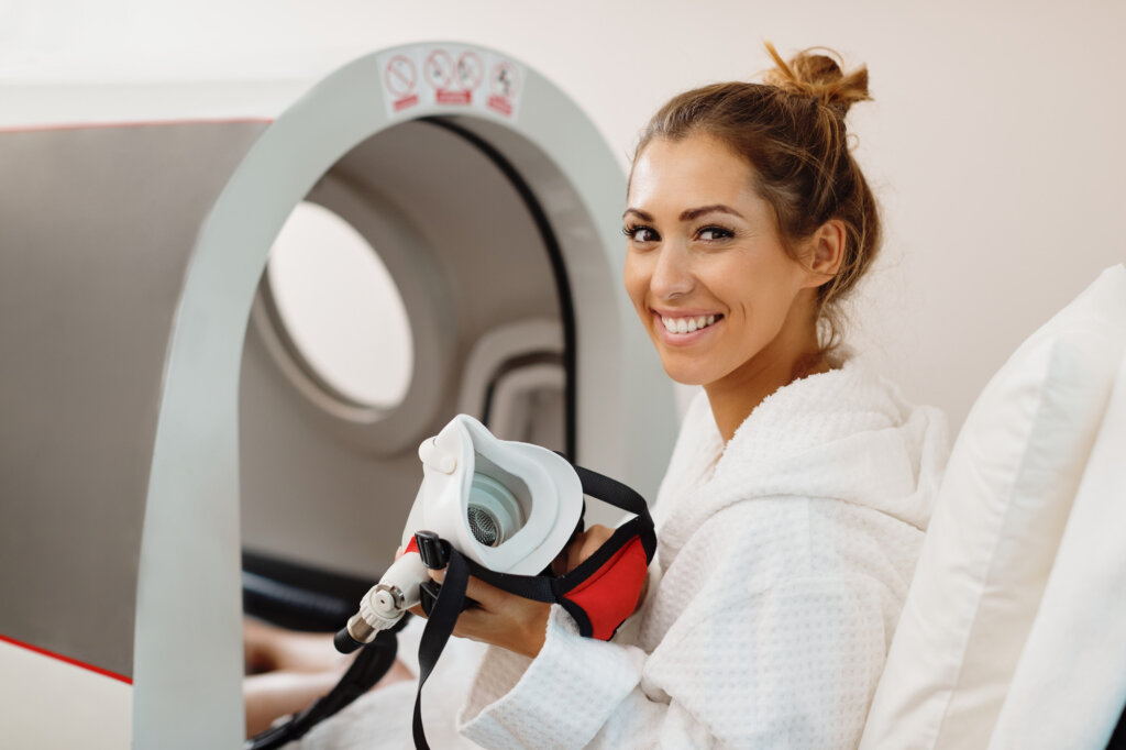 Young happy woman using oxygen mask during hyperbaric oxygen therapy at health spa.