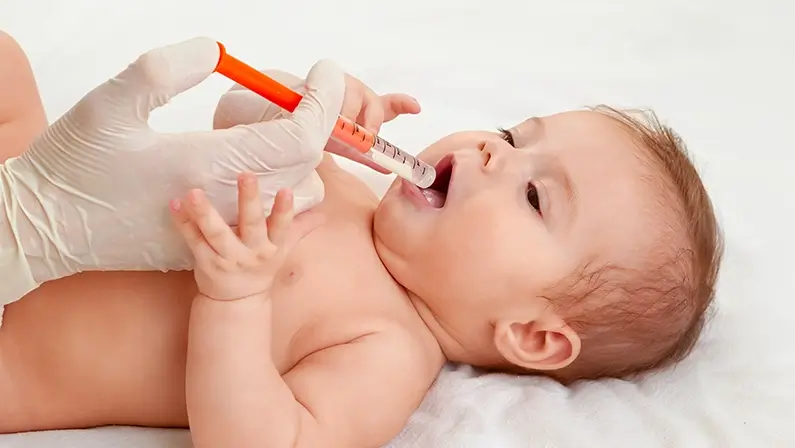 Doctor giving remedy to baby. Little baby is taking medicine helping by a syringe handled by doctor. Regular examining to pediatrician at hospital. Baby health concept