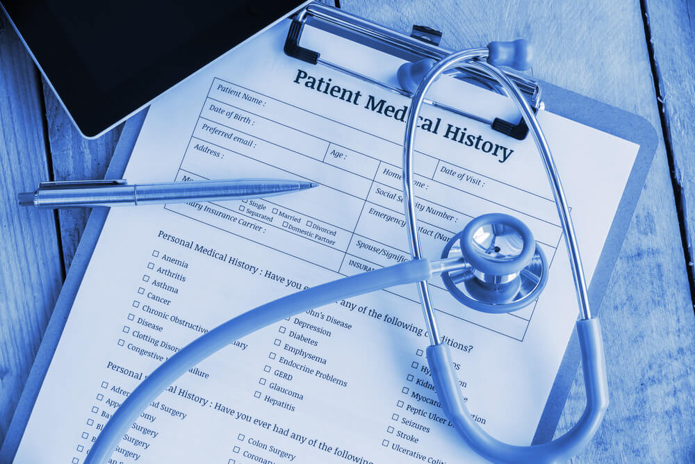 Patient medical history on a clipboard with stethoscope and a blue ballpoint pen, putting on a physician's table. Blank form waiting to be filled and reviewed / examined by nurse / clinical assistant.
