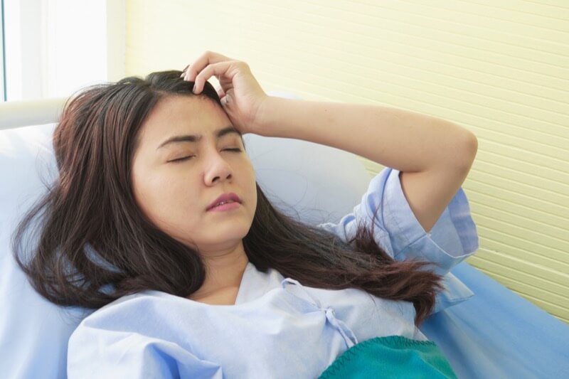 Asian woman, unhappy patient suffering from a strong headache and get high fever from infections with seasonal flu and cold while lying in the hospital room. Health care, medical insurance concept.