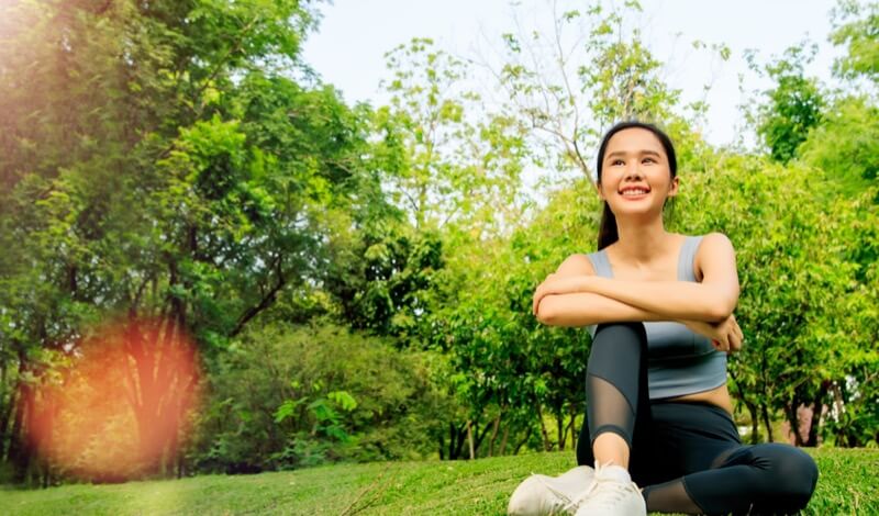 Young beautiful asian woman healthy and health conscious wearing sportswear for exercising in the park sitting relaxing looking at the peace of nature good mood happy feeling free positive.