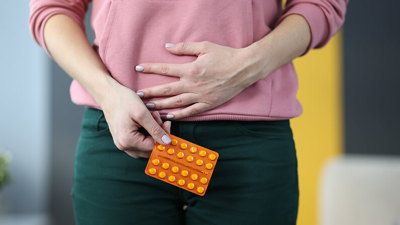 Woman with pills in hands holding lower abdomen at home closeup. Treatment of reproductive system of women concept