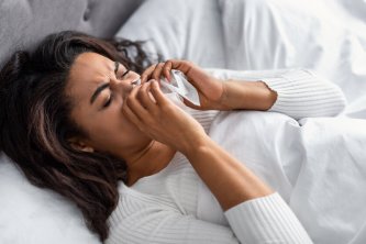 Sick black woman suffering from running stuffy nose and sore throat. Upset ill African American lady lying in bed, blowing her nose using paper napkin tissue, banner. Cold And Flu Concept