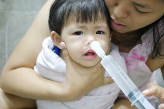 Asian mom rinsing her baby's stuffy nose using a syringe of saline water - effective home remedy for clearing a baby's clogged nose